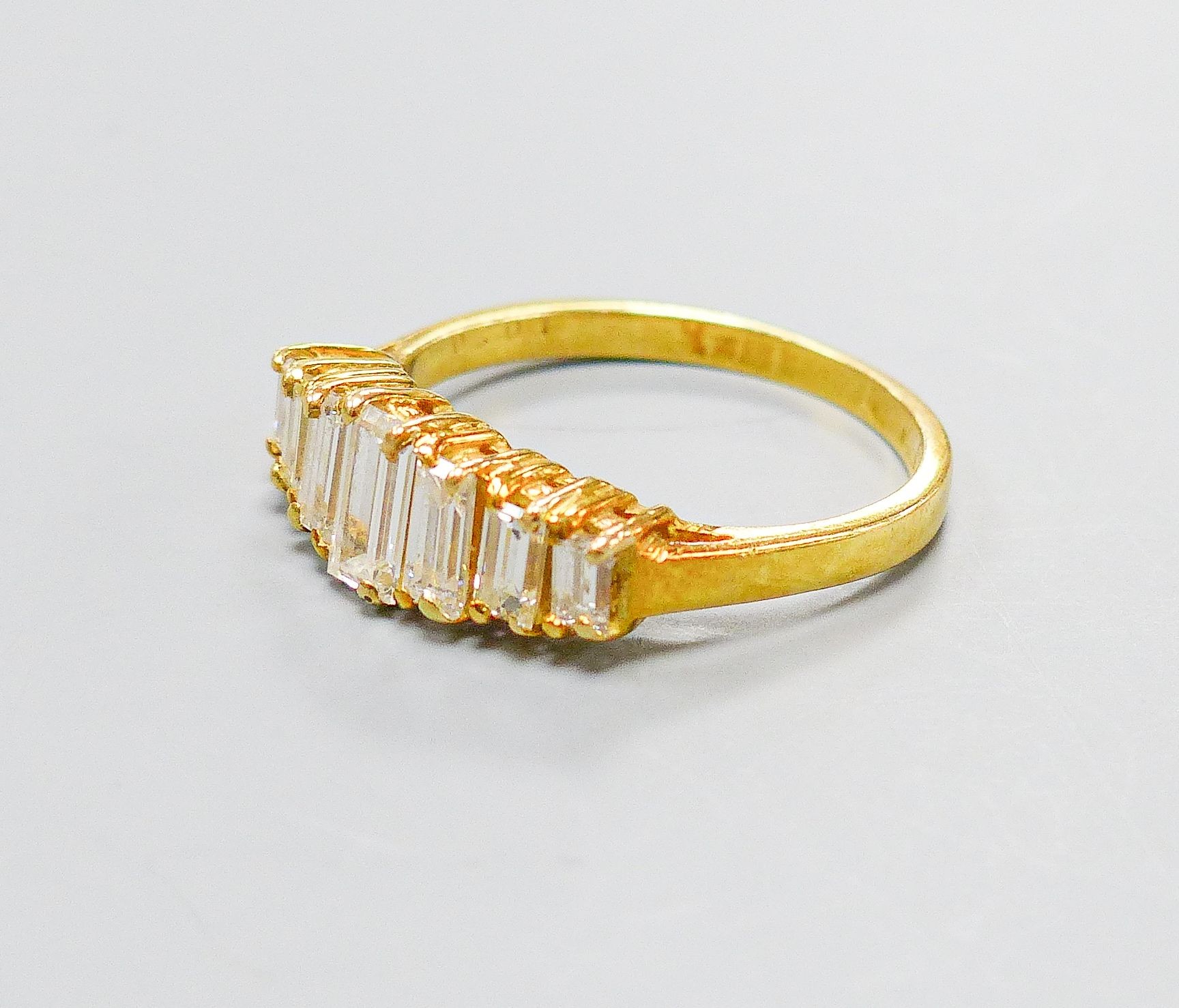 A modern 18ct gold and graduated seven stone baguette cut diamond set half hoop ring, size O, gross weight 4.1 grams.
